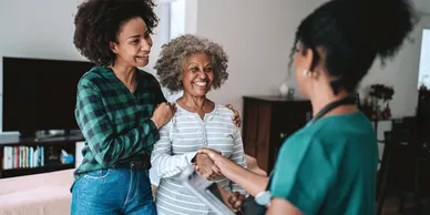 Old lady shaking hands with the therapist with her daughter beside.