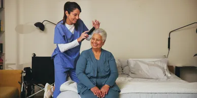 An old woman getting her hair combed by a caregiver.