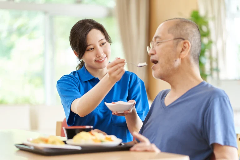 A caregiver who assists the elderly man in eating his meal.