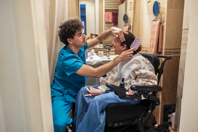 Caregiver assisting the woman in the wheelchair by combing her hair.